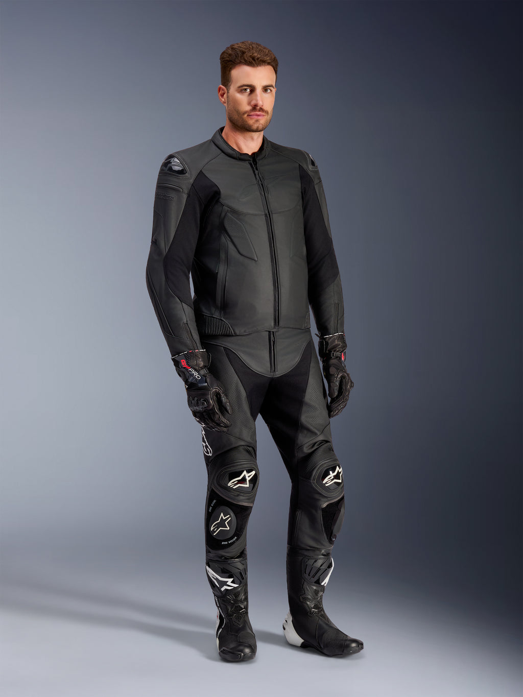 Mandlig model iført Alpinestars Caliber læderjakke i sort, kombineret med matchende sorte lædermotorcykelbukser, racinghandsker og støvler, som viser et komplet sportsligt motorcykeloutfit til vej.
