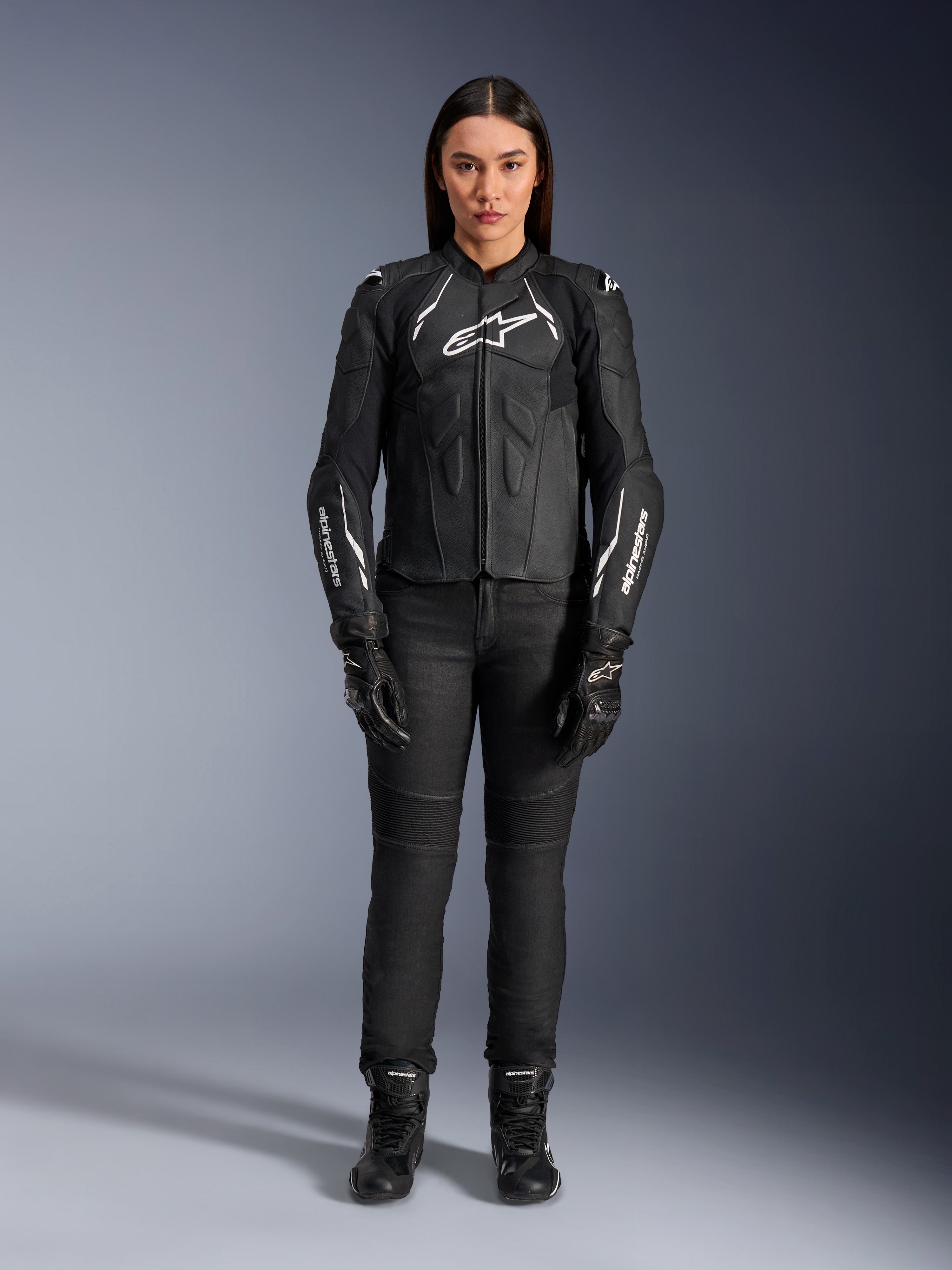 Alpinestars Stella Dusk læderjakke til kvinder, sort og hvid, båret af en model med matchende sorte bukser og støvler, set forfra, med hvide Alpinestars-logoer på brystet og ærmerne, beskyttelsesudstyr i premium okselæder til kvinder