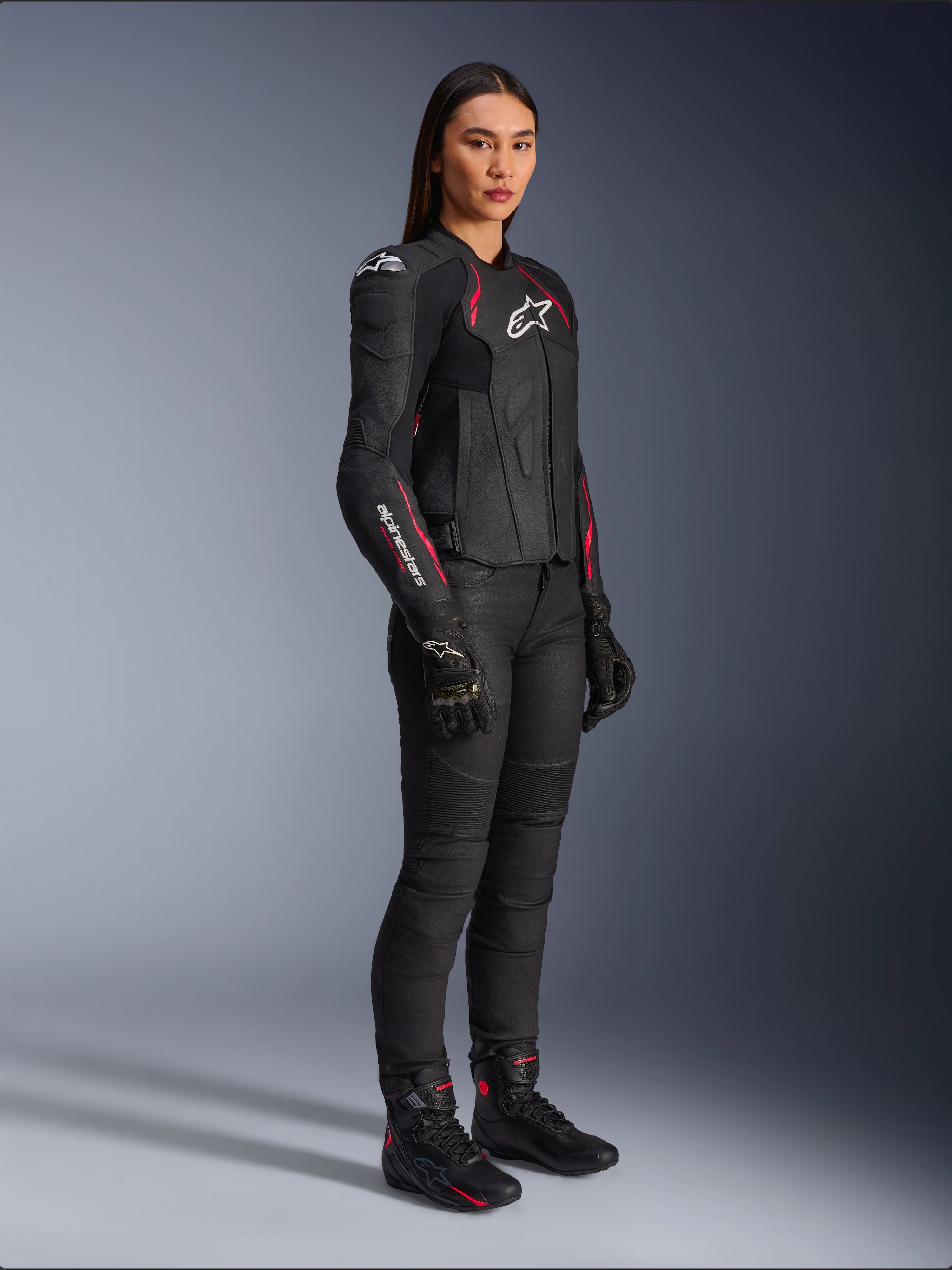 Alpinestars Stella Dusk læderjakke til damer, sort, Diva Pink og hvid, båret af en kvindelig model med sorte motorcykelbukser og støvler, strømlinet læderkonstruktion med lyserøde detaljer og hvidt logo
