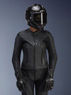 Alpinestars Stella GP Plus V4 læderjakke til kvinder i Black Black, vist med en sort kulfiberhjelm og racerhandsker, strømlinet læderkonstruktion med diskret branding på brystet, skræddersyet silhuet til kvindelige kørere, professionelt sportsmotorcykeludstyr