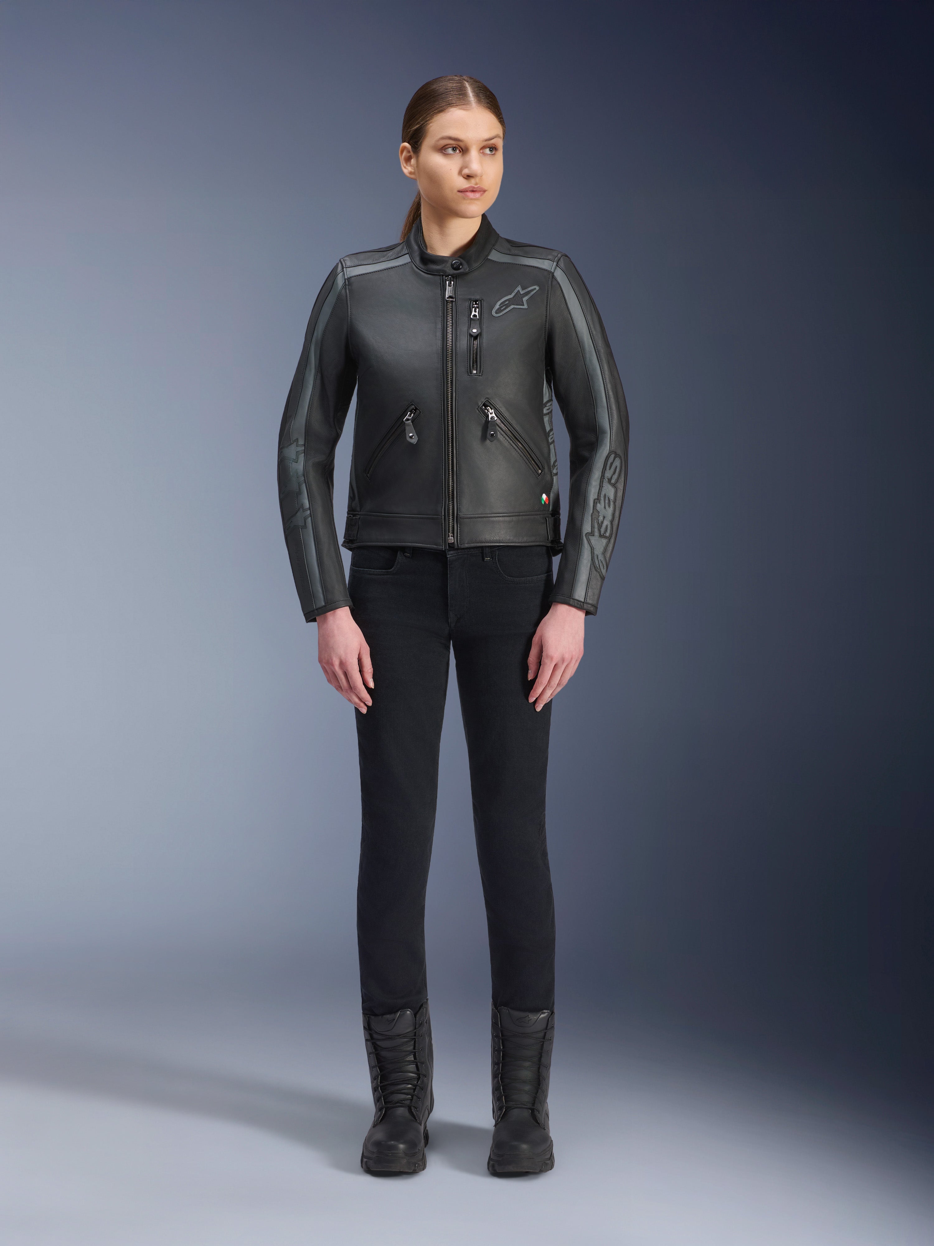 Alpinestars Stella Dyno læderjakke, motorcykeljakke til damer, Black Tar Gray Dark Gray, fuld kropsvisning i studie af en model iført jakken med sorte slim-fit bukser og sorte støvler, konstruktion i okselæder med grå detaljer og diskret Alpinestars-branding på bryst og ærmer.