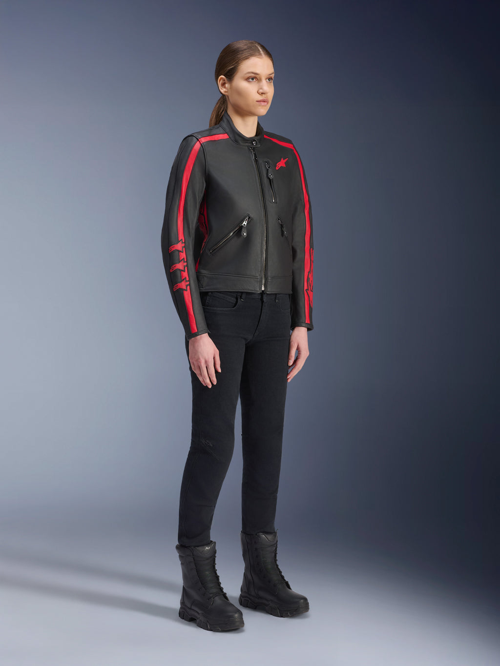 Kvindelig model iført Alpinestars Stella Dyno læderjakke i Black Haute Red, kombineret med sorte bukser og støvler, lædermotorcykeljakke i heritage-stil med røde striber på ærmerne og rødt logo, urban- og landevejskøreudstyr til kvinder