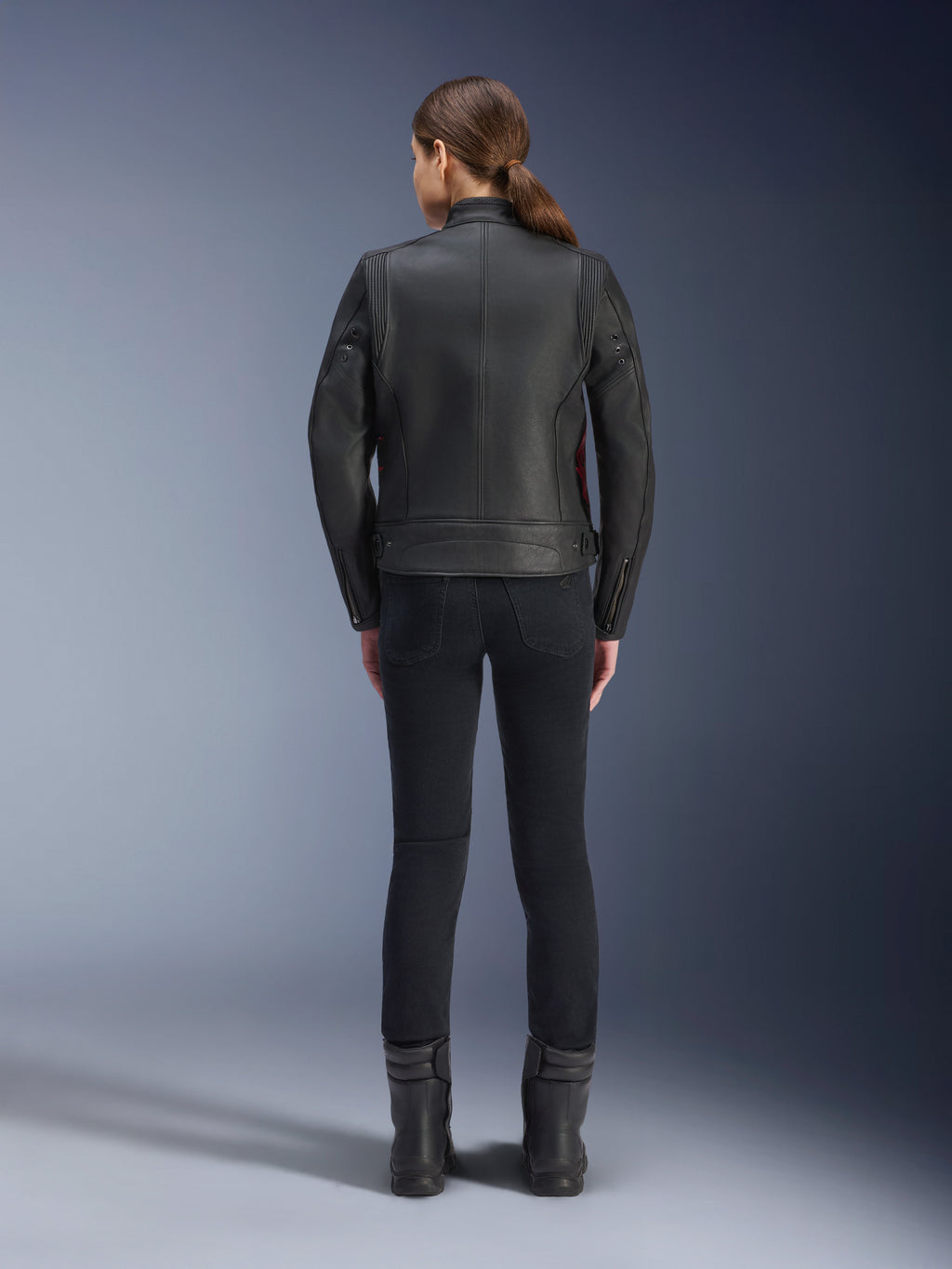Alpinestars Stella Dyno læderjakke set bagfra, kvinde iført sort jakke med Haute Red-detaljer, kombineret med sorte slim-fit bukser og sorte støvler, moderne heritage lædermotorcykeljakke-design