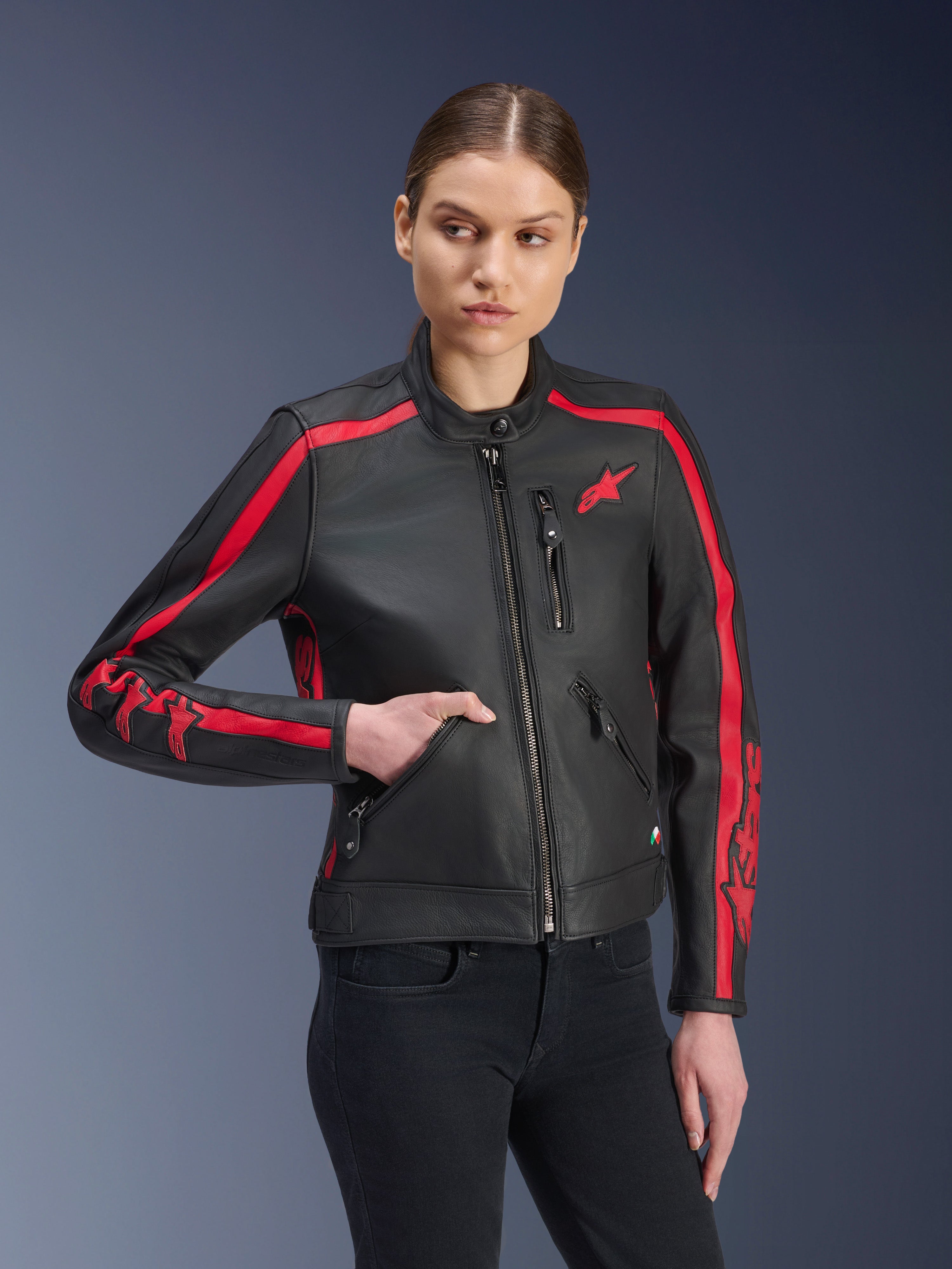 Alpinestars Stella Dyno læderjakke, dame motorcykeljakke, Black Haute Red, båret af en model med sorte jeans, med røde racerstriber på skuldre og ærmer med markant branding, premium læderkonstruktion, heritage-inspireret design til urban kørsel