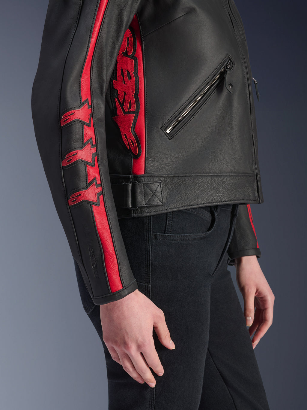Alpinestars Stella Dyno læderjakke, motorcykeljakke til kvinder, sort og Haute Red, set fra siden båret af en model, med røde racerstriber med stjernelogoer på ærmet og et stort rødt logo på siden, førsteklasses bovinelæder, urban kørestil