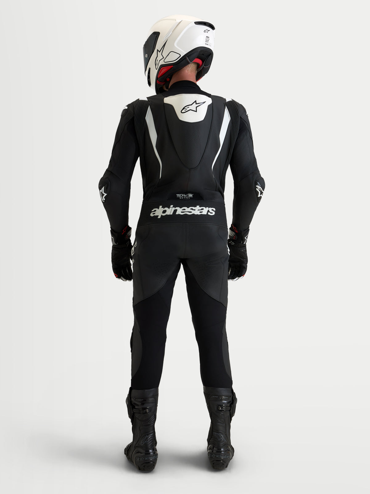 Alpinestars Missile V3 læderdragt, 1-delt motorcykelracerdragt, sort og hvid, med aerodynamisk speed hump og Alpinestars-branding set bagfra på kører med hvid hjelm og sorte støvler