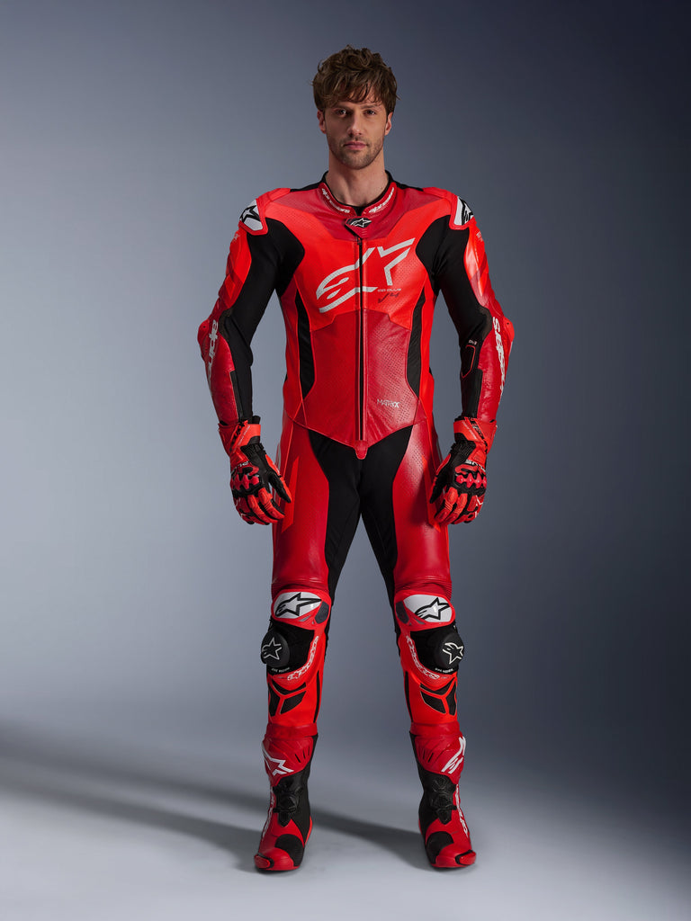 Model wearing the Alpinestars GP Plus V4 Sprint One Piece Leather Suit, Red Fluo Mid Red and White, featuring black and white accents, worn with matching racing gloves and boots, sporty design with large chest logo and perforated leather panels for ventilation.