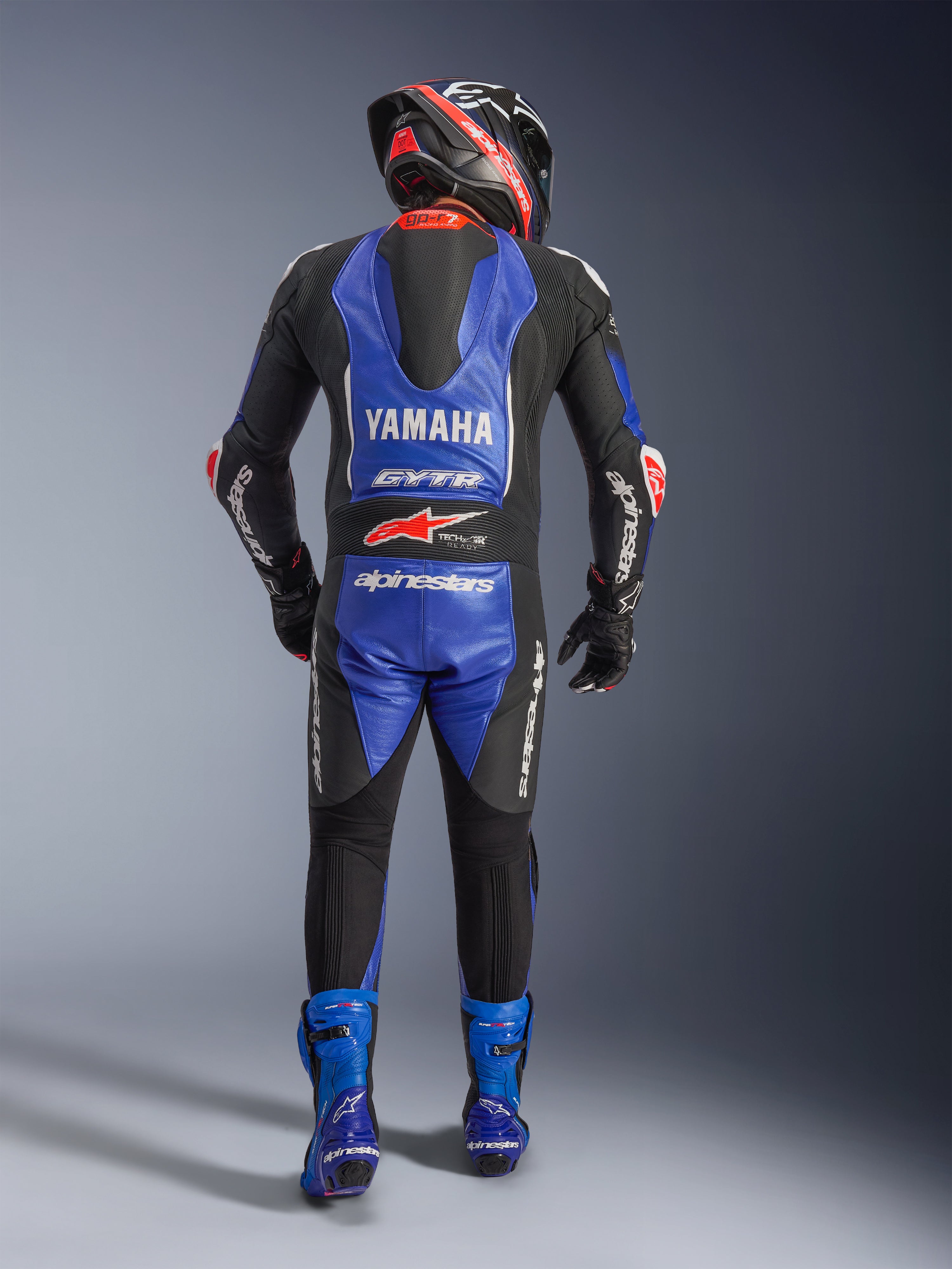 Alpinestars Yamaha GP-R7 læderdragt i ét stykke, motorcykelrytter set bagfra i fuldt racerudstyr, metallisk blå og sort med hvide og røde detaljer, Yamaha- og GYTR-branding på den aerodynamiske pukkel, båret med matchende blå støvler og racerhjelm