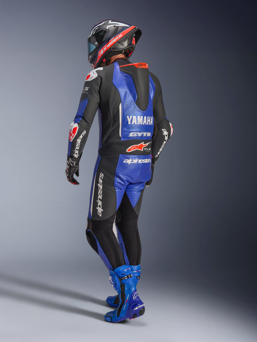 Alpinestars Yamaha GP-R7 læderdragt, metallisk blå, sort og hvid, set bagfra med aerodynamisk race-pukkel og Yamaha-branding, båret med matchende blå racerstøvler og hjelm, professionel performance-læderdragt til banekørsel