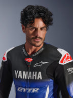Nærbillede af en mand iført Alpinestars Yamaha GP-R7 1PC læderdragt, metallic blå og sort med hvid YAMAHA og GYTR branding, perforeret læder, hvide skulder-sliders med røde stjernelogoer, Tech-Air Ready, professionelt motorcykel-racerudstyr.