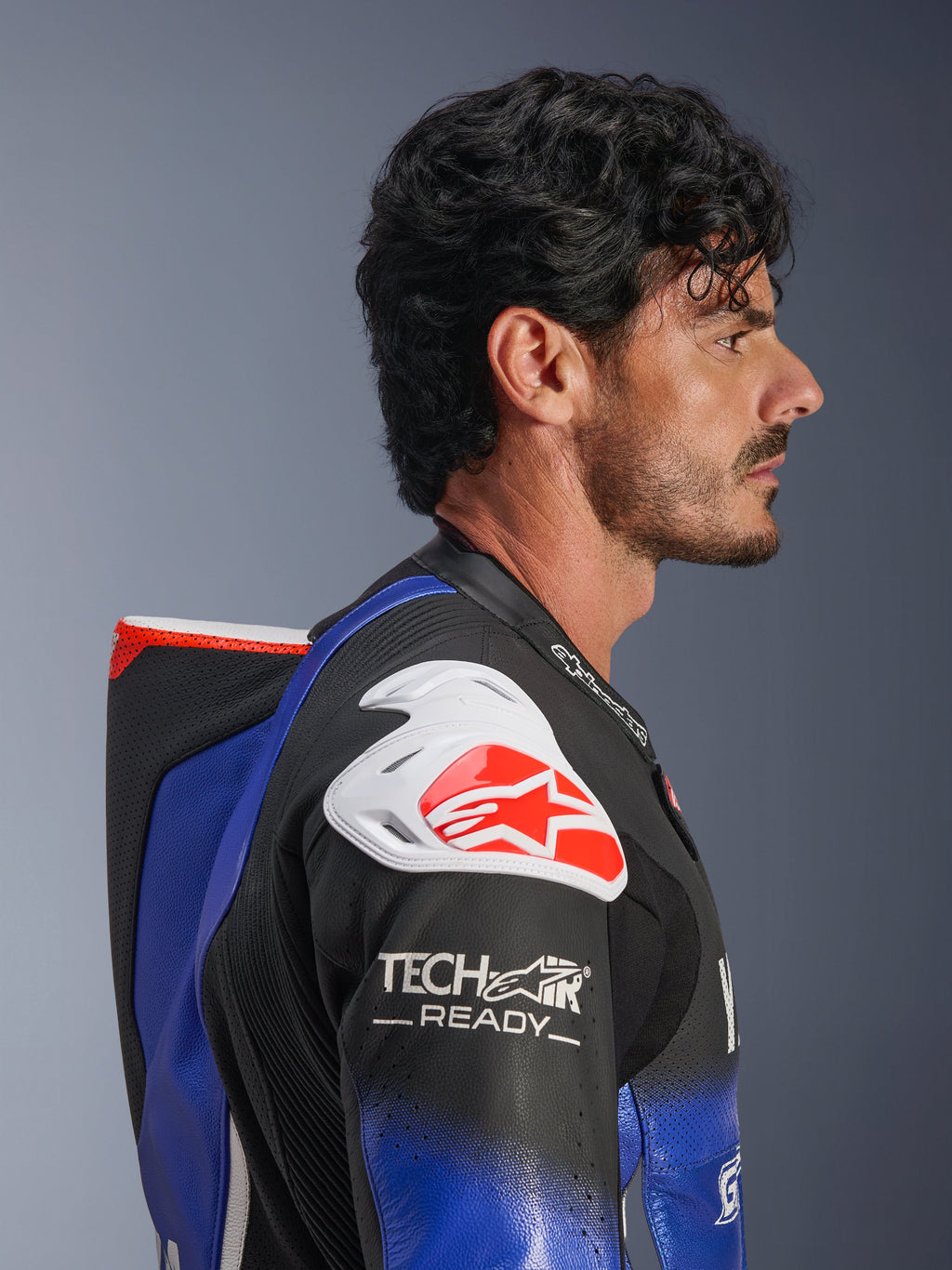 Alpinestars Yamaha GP-R7 læderdragt i ét stykke, metallic blå og sort med hvide og røde detaljer, sideprofil der fremhæver den aerodynamiske pukkel og hvid skulderbeskyttelse med rødt Alpinestars-logo, Tech-Air Ready-branding på ærmet, førsteklasses perforeret racelæder.
