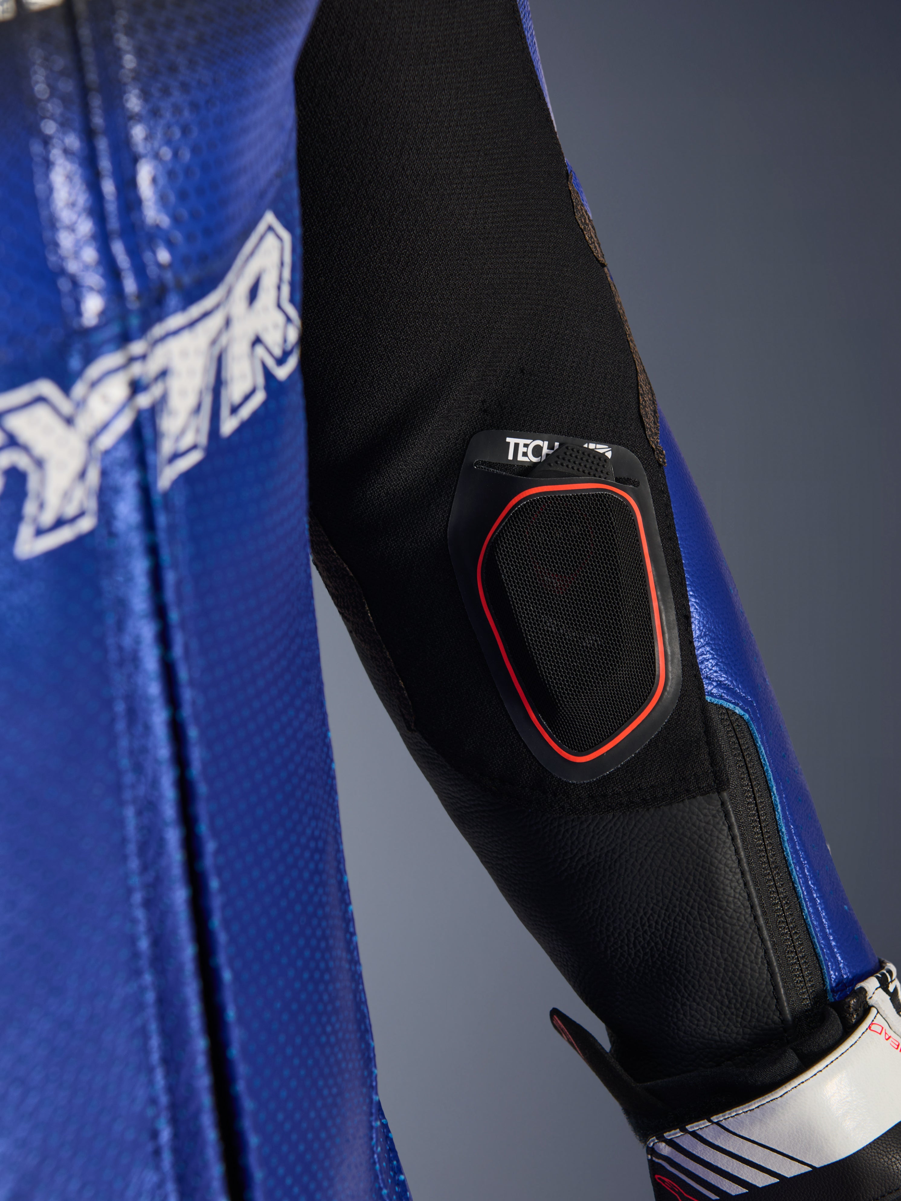 Nærbillede af underarmen på Yamaha GP-R7 læderdragten i ét stykke, der viser den integrerede Tech-Air 10 Bluetooth-displaylomme med rød kant, metallisk blåt perforeret læder og sorte strækstofindsatser til racing-ydeevne.