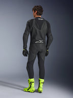 Alpinestars GP Force V2 læderdragt - 1-piece, sort, set bagfra båret af en model, med en aerodynamisk speed hump og Tech-Air Ready-branding, stylet med sorte handsker og klare fluorescerende gule racestøvler, professionelt baneudstyr