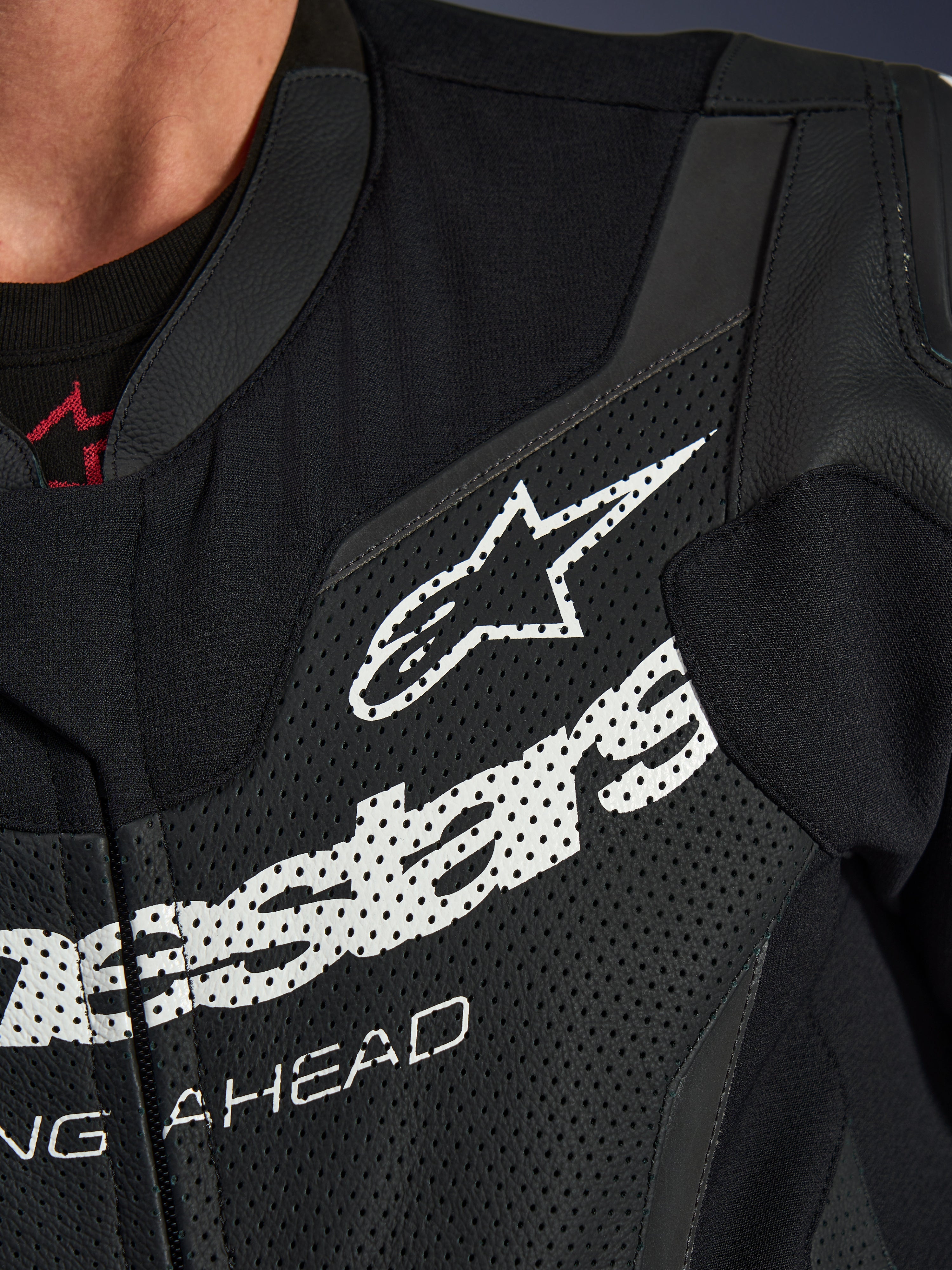 Alpinestars GP Force V2 læderdragt 1-piece, nærbillede af brystområdet, sort perforeret læder med stort hvidt Alpinestars-logo, teknisk sportskøreudstyr, detaljeret tekstur og branding