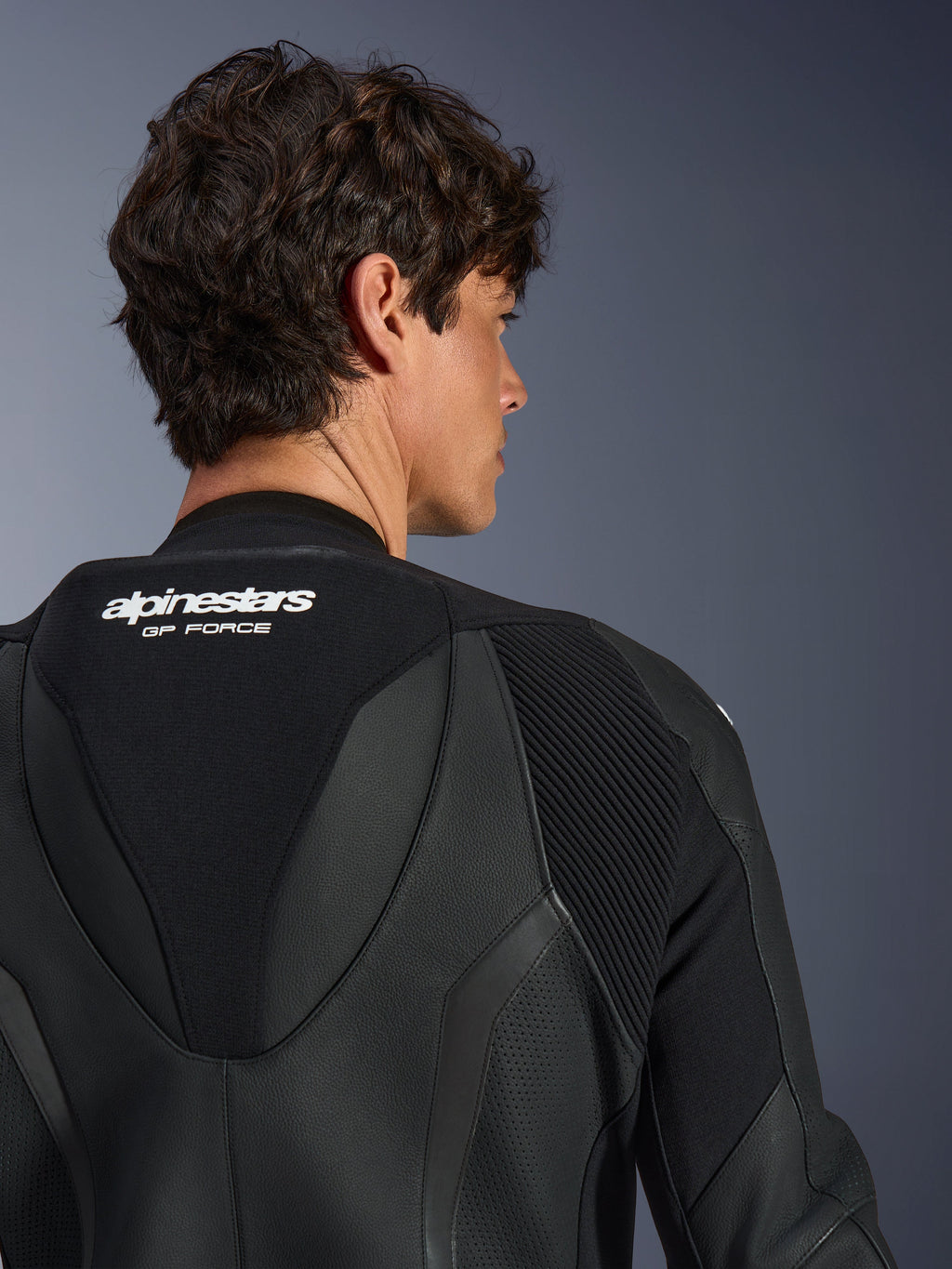 Alpinestars GP Force V2 Læderdragt 1-piece, sort, nærbillede af den øvre ryg og aerodynamisk speed hump, med hvid branding, perforerede lædersektioner og harmonika-strækpaneler til højtydende racing.