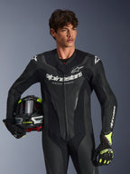 Alpinestars GP Force V2 læderdragt, 1-delt sort motorcykel-racerdragt med perforerede læderpaneler og hvidt logo-branding, båret af en model, der holder en hjelm og matchende handsker, studiebelysning