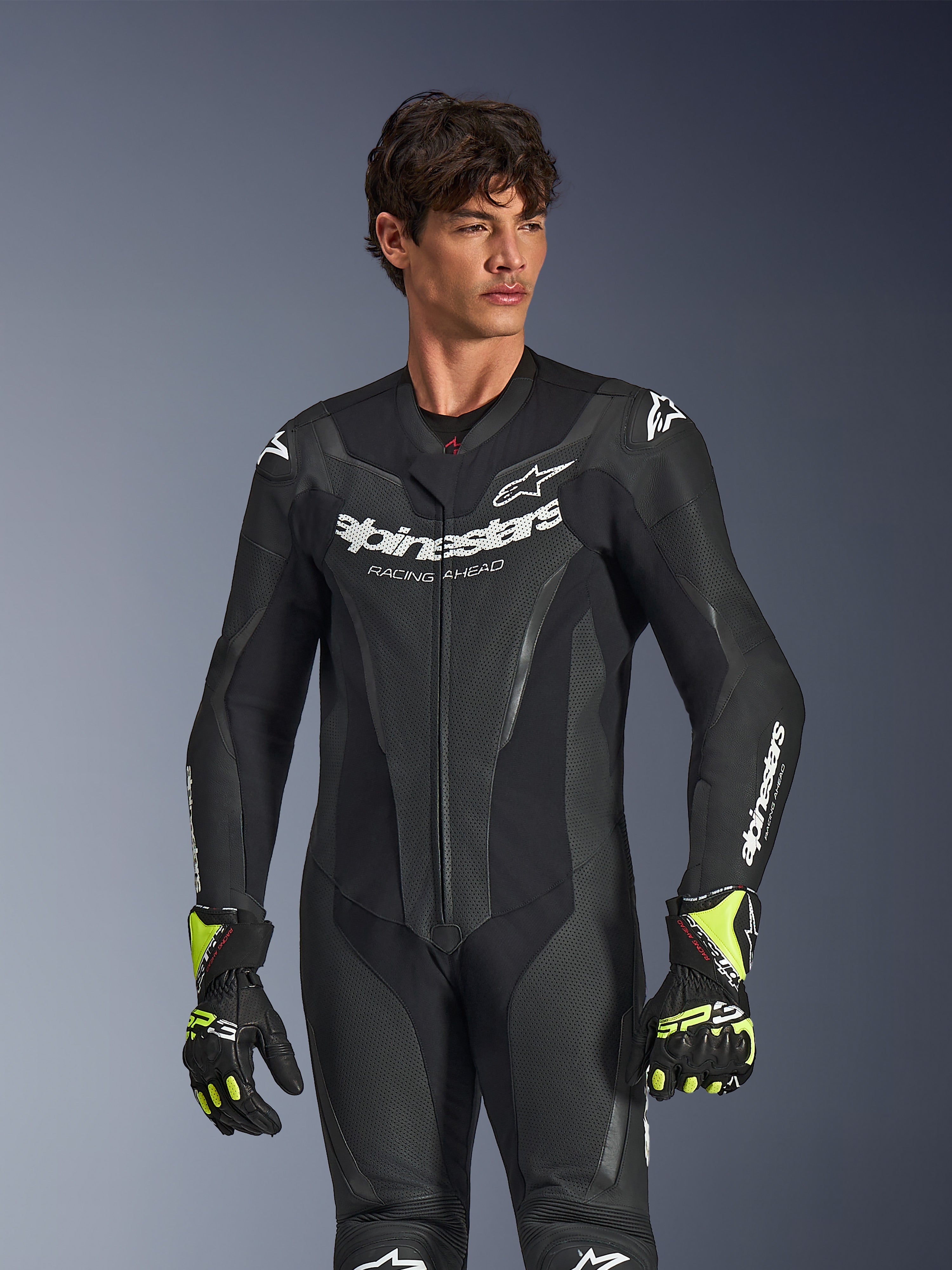Alpinestars GP Force V2 læderdragt 1-piece, sort, hvid Alpinestars-branding og logo, perforerede læderpaneler til ventilation, båret af en mandlig model med sorte og neongule handsker, højtydende motorcykelracerudstyr