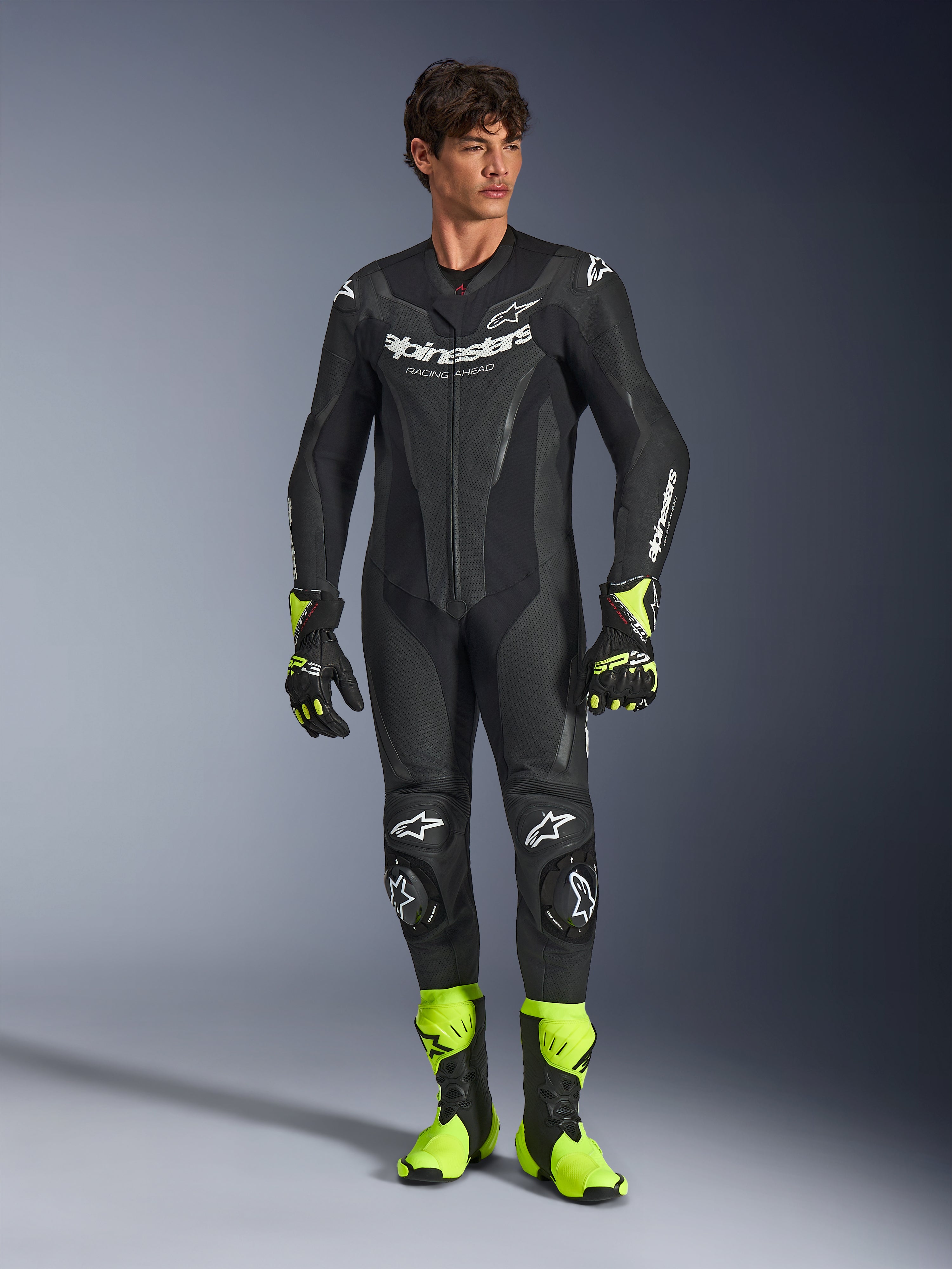 Alpinestars GP Force V2 læderdragt, 1-piece sort motorcykelracingdragt, båret med neongule støvler og handsker, med hvide logoer og perforeret læder, strømlinet tætsiddende design til banedage