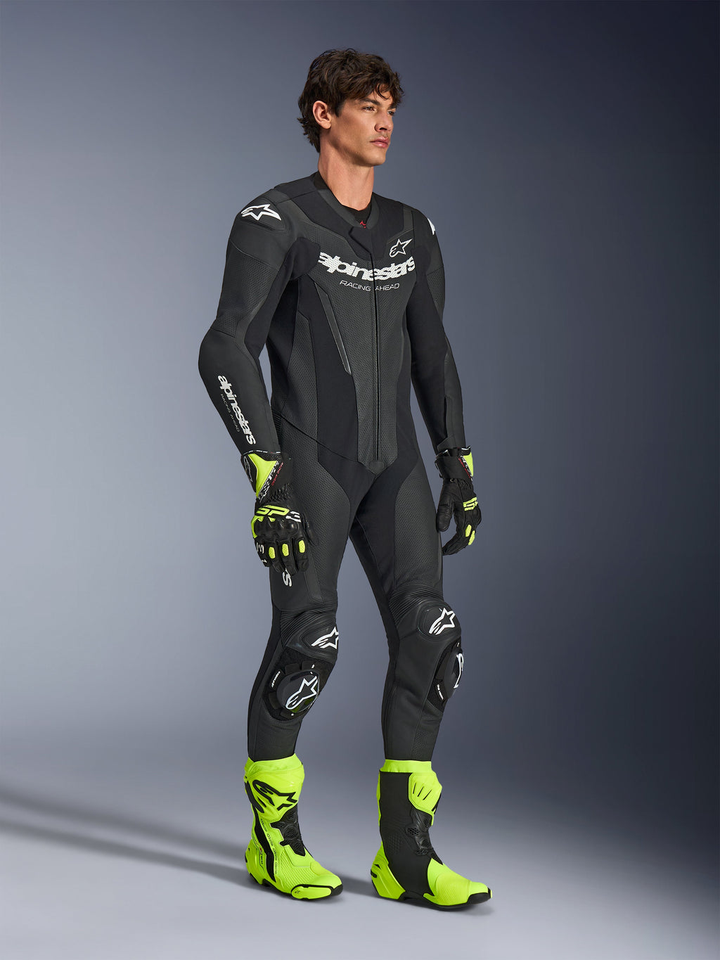 Mand iført Alpinestars GP Force V2 1-piece læderdragt i sort, med hvidt Alpinestars branding, perforerede læderområder og integreret beskyttelse, stylet med neongule og sorte racingstøvler og handsker