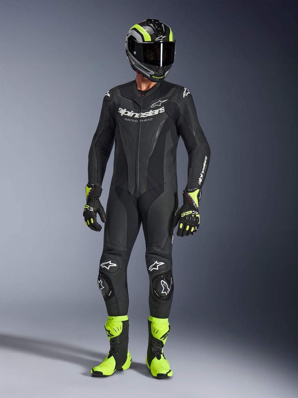 Motorcykelrytter iført Alpinestars GP Force V2 læderdragt i sort, 1-delt læderdragt med hvid branding, kombineret med en sort og neongul racinghjelm, handsker og støvler, professionelt banekørselsudstyr på en grå studiebaggrund