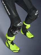 Alpinestars GP Force V2 læderdragt, 1-delt sort læderdragt, tætbillede af ben og knæ med hvide logo-sliders, harmonika-strækpaneler, båret med neongule racerstøvler, højtydende motorcykel-racerudstyr