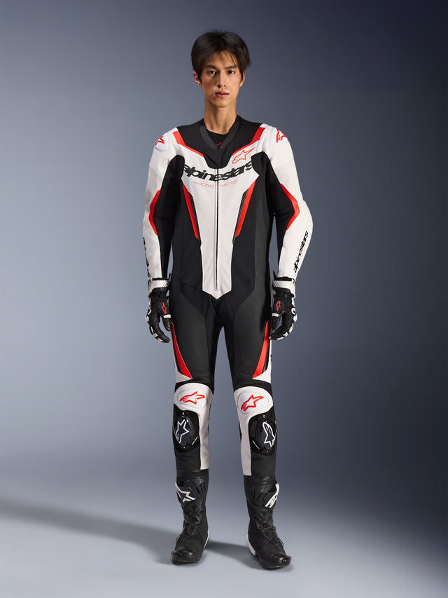 Alpinestars GP Force V2 Leather Suit - 1Piece, White Black Red Fluo, one-piece leather motorcycle racing suit, front view on model, featuring perforated panels and red accents, bold Alpinestars branding on chest, styled with professional racing boots and gloves