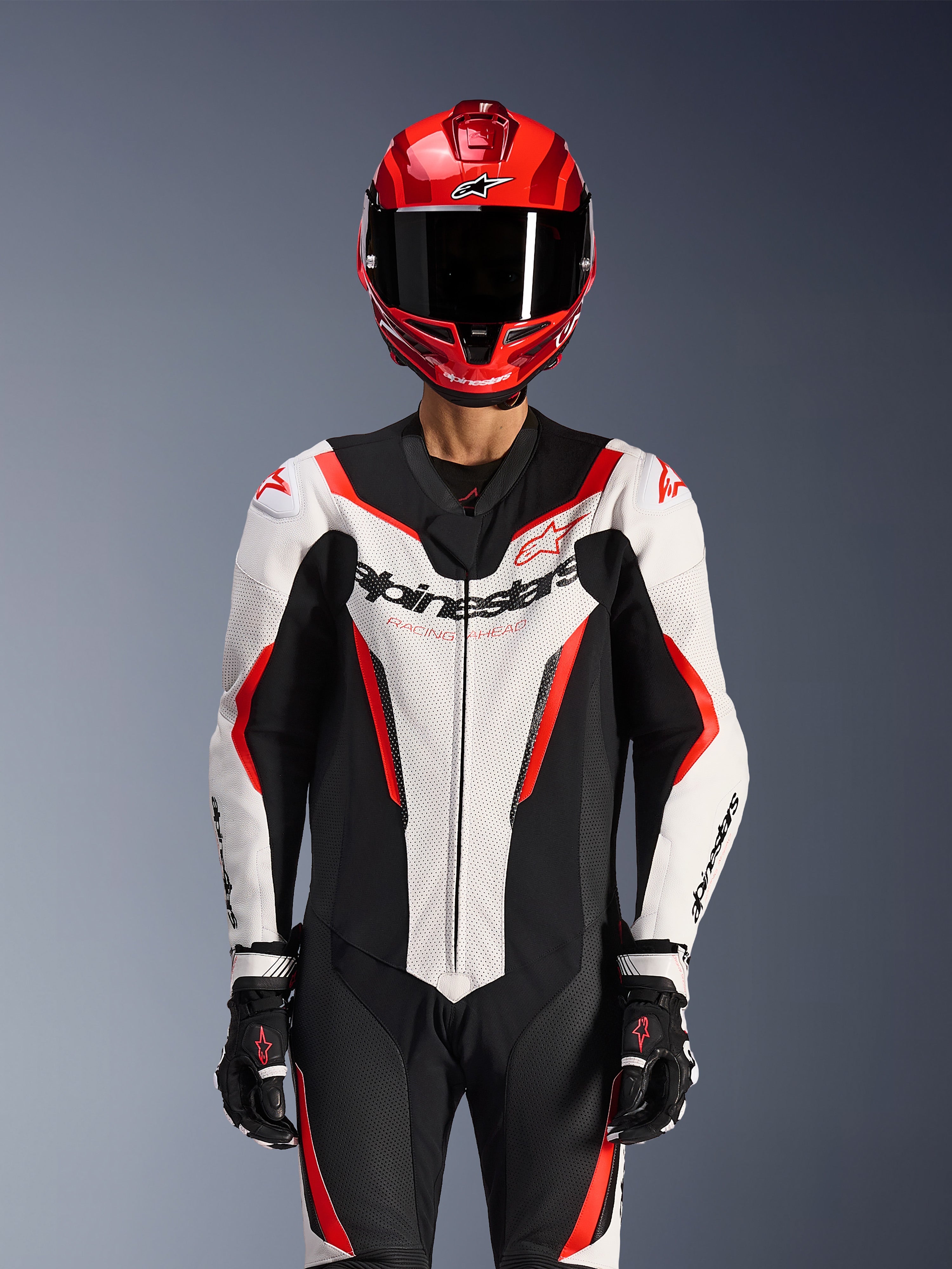 Alpinestars GP Force V2 Leather Suit - 1Piece, White Black Red Fluo, worn with red full-face helmet and black racing gloves, featuring perforated leather panels and bold Alpinestars branding on the chest, professional performance gear for motorcycle racing