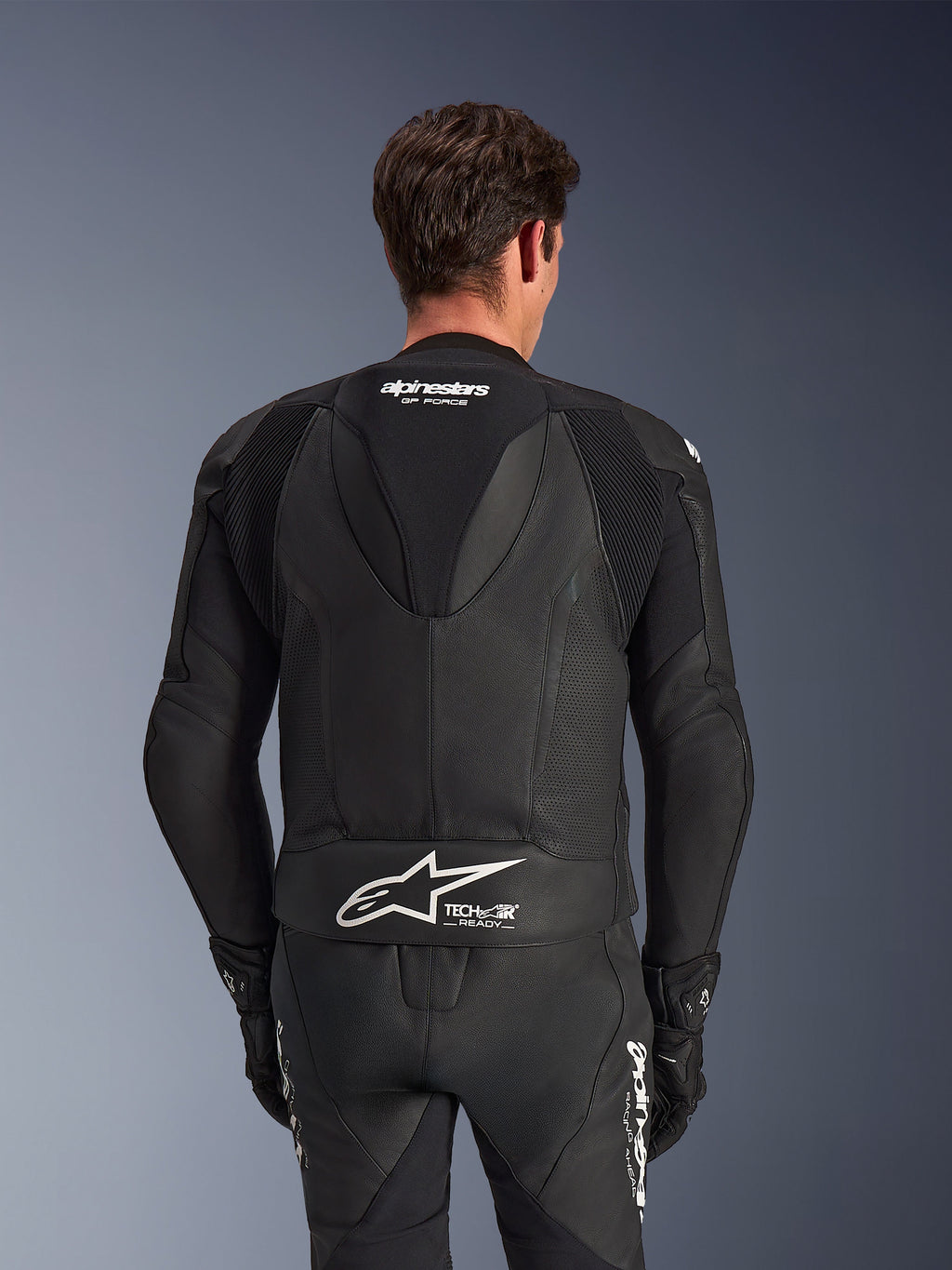 Alpinestars GP Force V2 læderdragt, 2-delt, sort, set bagfra på kører, med perforerede læderpaneler, aerodynamisk rygpukkel med GP Force-branding og hvidt Alpinestars-logo med Tech-Air Ready-tekst på lænden.