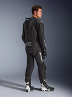 Mandlig model iført Alpinestars GP Force V2 2-delt læderdragt i sort med hvide logoer, set bagfra i trekvart profil, der viser den aerodynamiske speed hump og Tech-Air Ready-branding, kombineret med sort-hvide racingstøvler og handsker, professionelt motorcykeludstyr til sport og banekørsel.