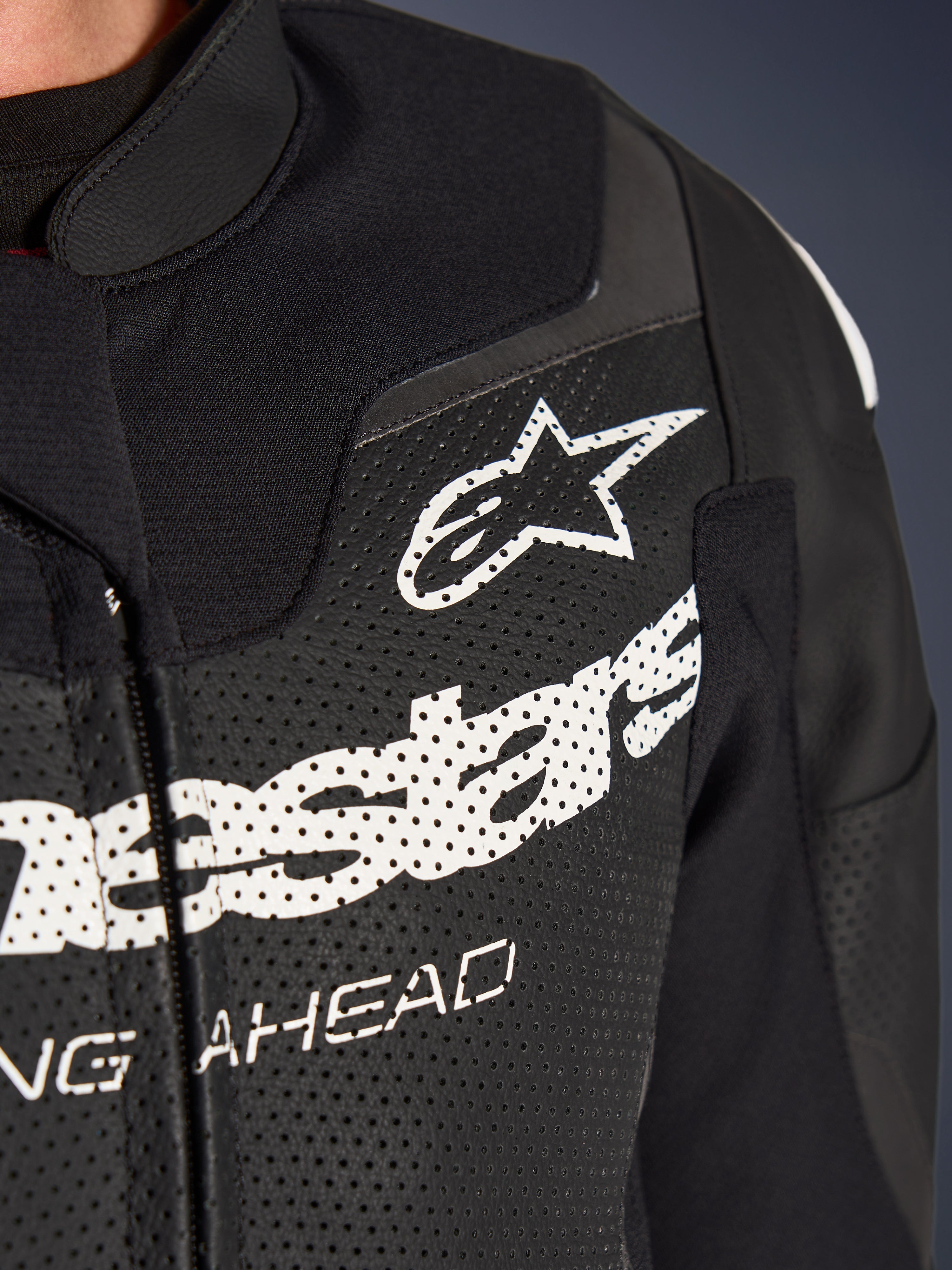 Alpinestars GP Force V2 todelt læderdragt, racing/sport motorcykeldragt, sort, nærbillede af perforeret læder på brystet med hvidt Alpinestars-logo og branding, der fremhæver ventilationshuller og tekstureret konstruktion.