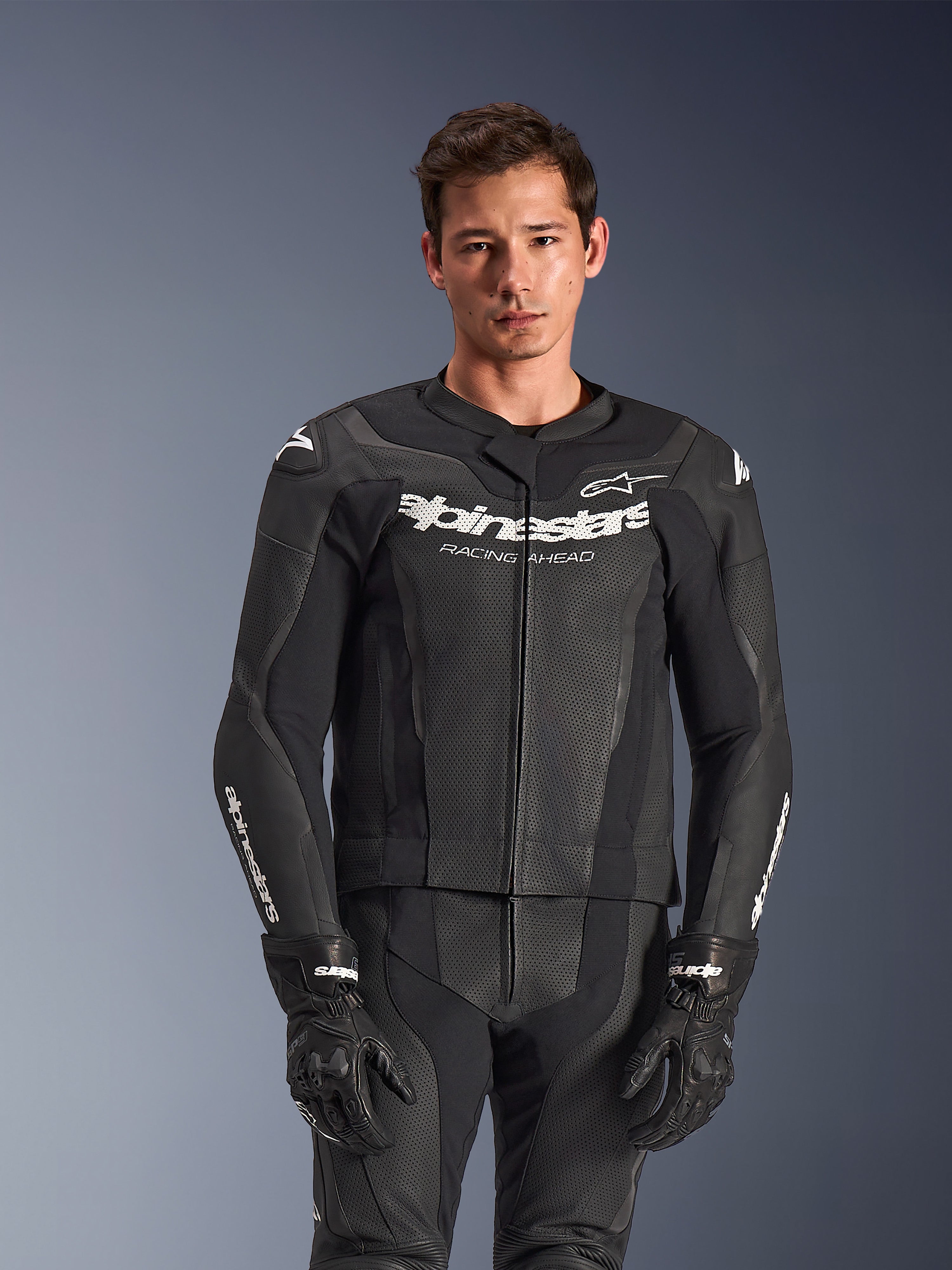 Alpinestars GP Force V2 2-delt læderdragt, sort, båret af model, med perforerede læderpaneler og hvidt 'Alpinestars Racing Ahead' logo på brystet, kombineret med sorte handsker, professionelt sportskøreudstyr