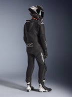 Alpinestars GP Force V2 2-delt læderdragt, sort, motorcykelrytter set bagfra i fuldt racerudstyr, med aerodynamisk fartpukkel, hvid branding og perforeret læder, kombineret med en kulfiberhjelm og sort-hvide racerstøvler