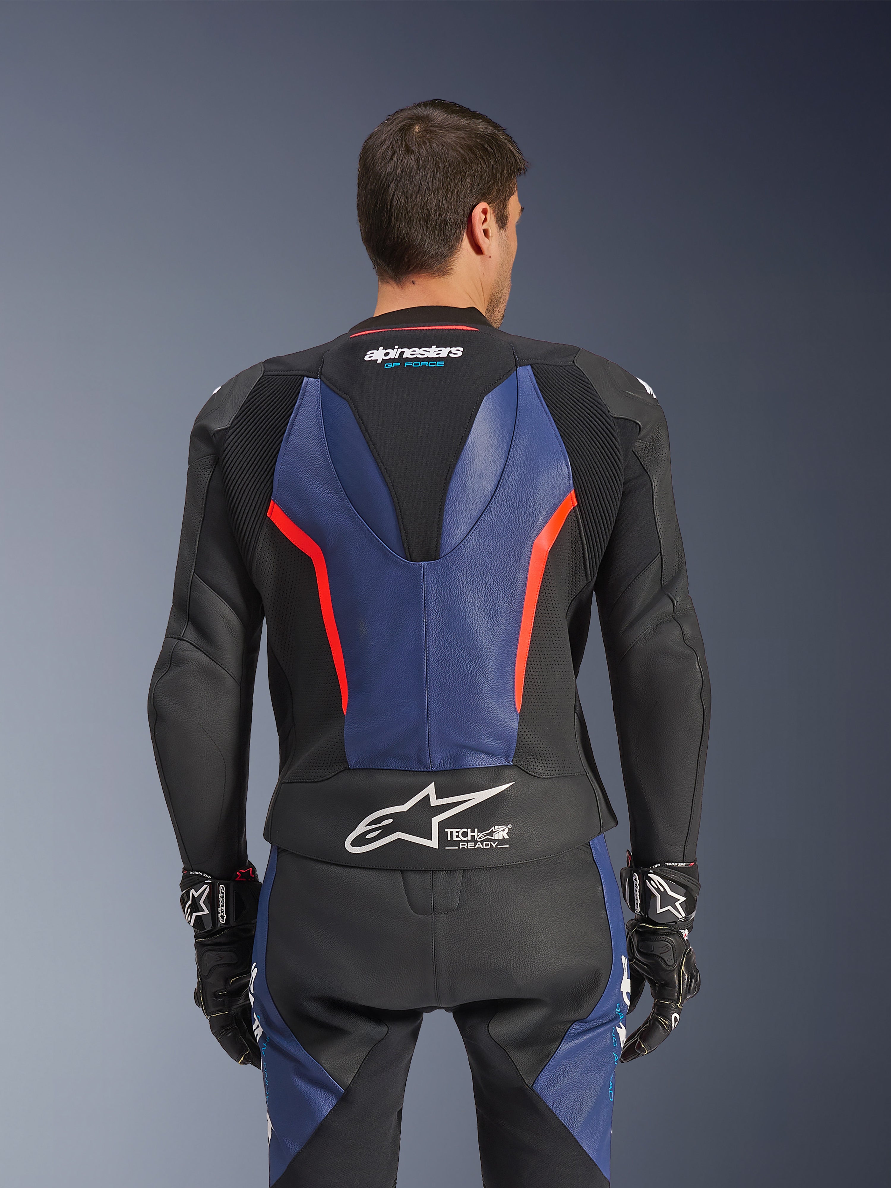 Alpinestars GP Force V2 Leather Suit 2-Piece, Back view, Black with Blue and Red Fluo accents, featuring perforated leather construction, Tech-Air Ready branding on the waist, and ergonomic stretch panels for racing performance.