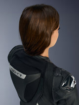 Close-up of the upper back and shoulder of the Alpinestars Stella GP-R7 1-Piece Leather Suit in Black, featuring the aerodynamic speed hump with 'GP-R7' branding, DFS RR shoulder protector with Alpinestars logo, and multi-directional leather stretch accordions.