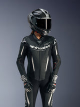Female rider in Alpinestars Stella GP-R7 1-Piece Leather Suit, Black with white accents, worn with a racing helmet and gloves, featuring perforated leather panels and Alpinestars 'Racing Ahead' branding on the chest, professional track gear.