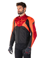 Alpinestars T-Jaws V4 vandtæt jakke, sort, fluorescerende rød og mørkerød, båret af en mandlig model med sorte bukser og motorcykelhandsker, aggressiv sportssilhuet med Alpinestars-logo på brystet, trekvart visning
