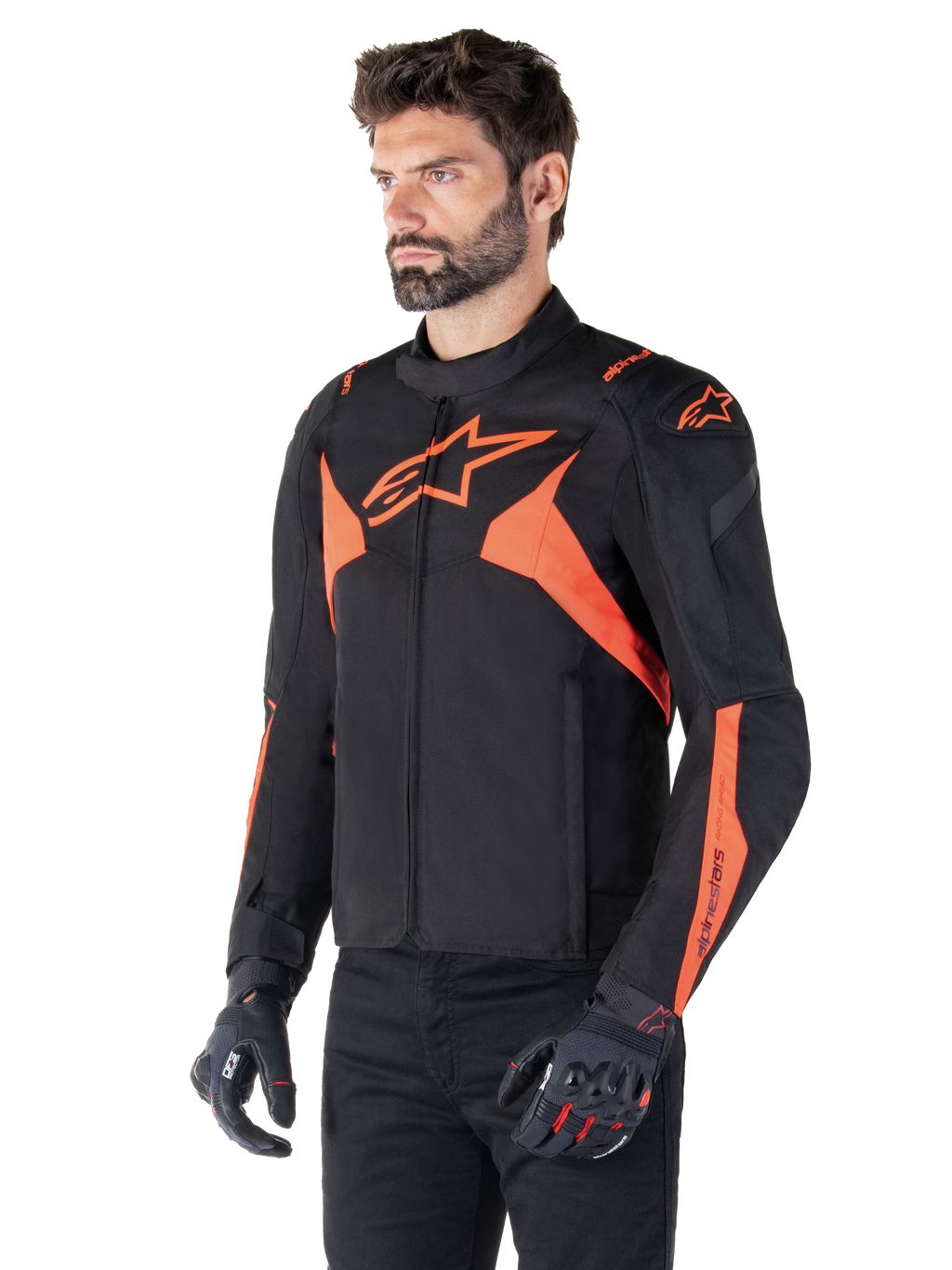 Alpinestars T-Jaws V4 vandtæt jakke, sort og neonrød, sportsmotorcykeljakke båret af en mandlig model, med markante orange stjernelogoer på bryst og skuldre, kombineret med sorte handsker og bukser