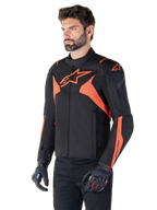 Alpinestars T-Jaws V4 vandtæt jakke, sort og neonrød, sportsmotorcykeljakke båret af en mandlig model, med markante orange stjernelogoer på bryst og skuldre, kombineret med sorte handsker og bukser
