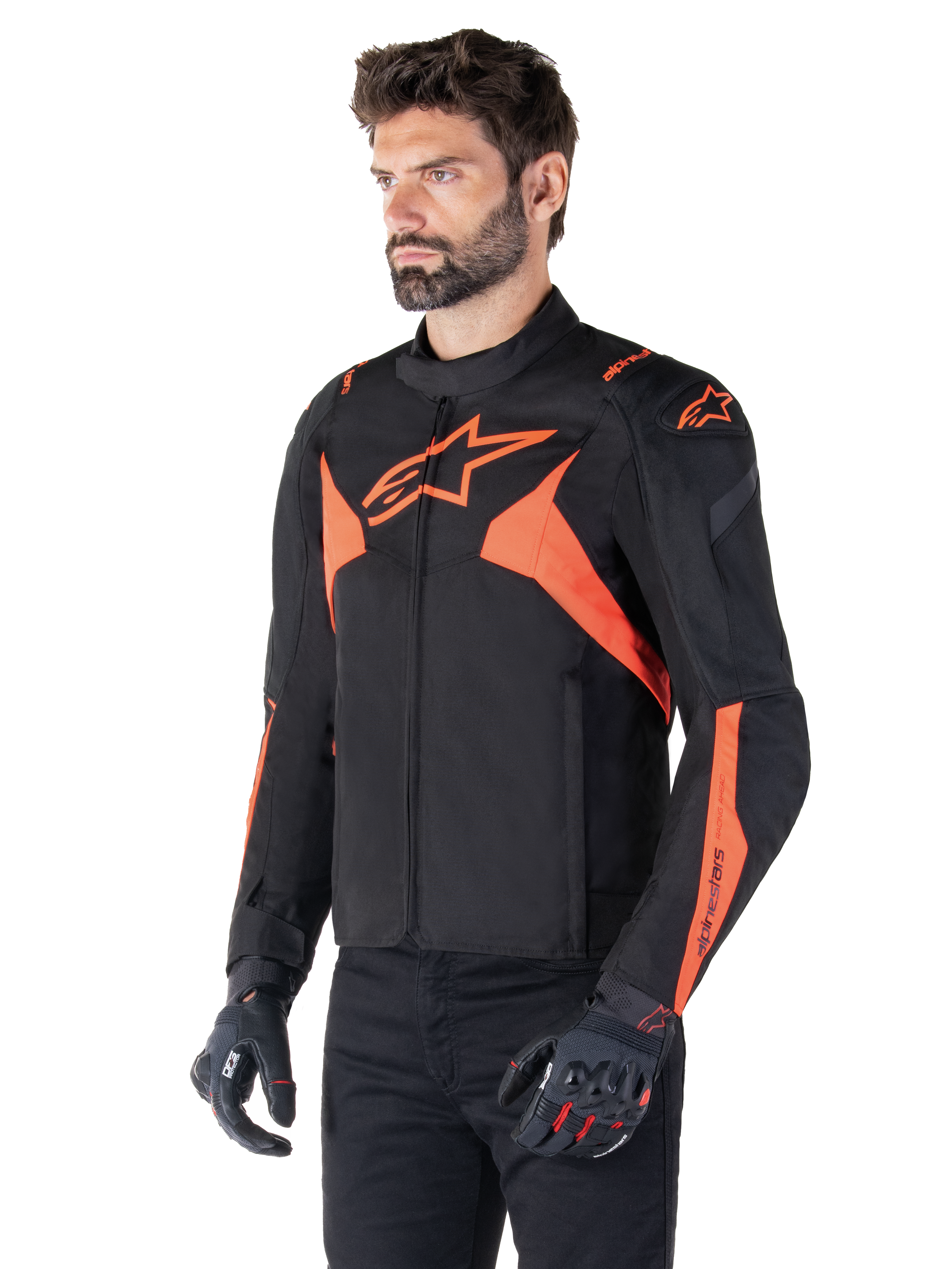 Alpinestars T-Jaws V4 vandtæt jakke, sort og neonrød, sportsmotorcykeljakke båret af en mandlig model, med markante orange stjernelogoer på bryst og skuldre, kombineret med sorte handsker og bukser