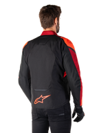 Set bagfra ses en mand iført Alpinestars T-Jaws V4 Waterproof-jakke i Black Red Fluo Dark Red, med markante røde detaljer på skuldre og ærmer, et fluorødt Alpinestars-logo på lænden, kombineret med sorte bukser og handsker.