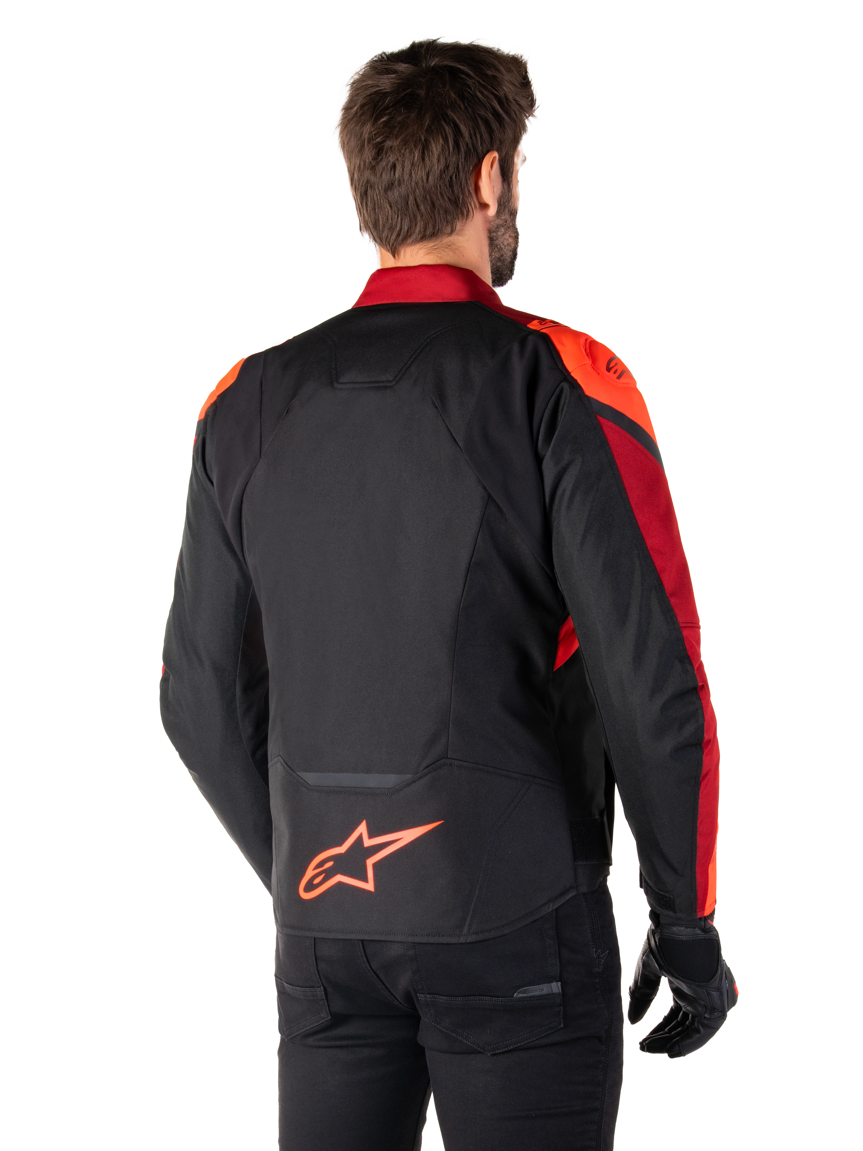 Set bagfra ses en mand iført Alpinestars T-Jaws V4 Waterproof-jakke i Black Red Fluo Dark Red, med markante røde detaljer på skuldre og ærmer, et fluorødt Alpinestars-logo på lænden, kombineret med sorte bukser og handsker.