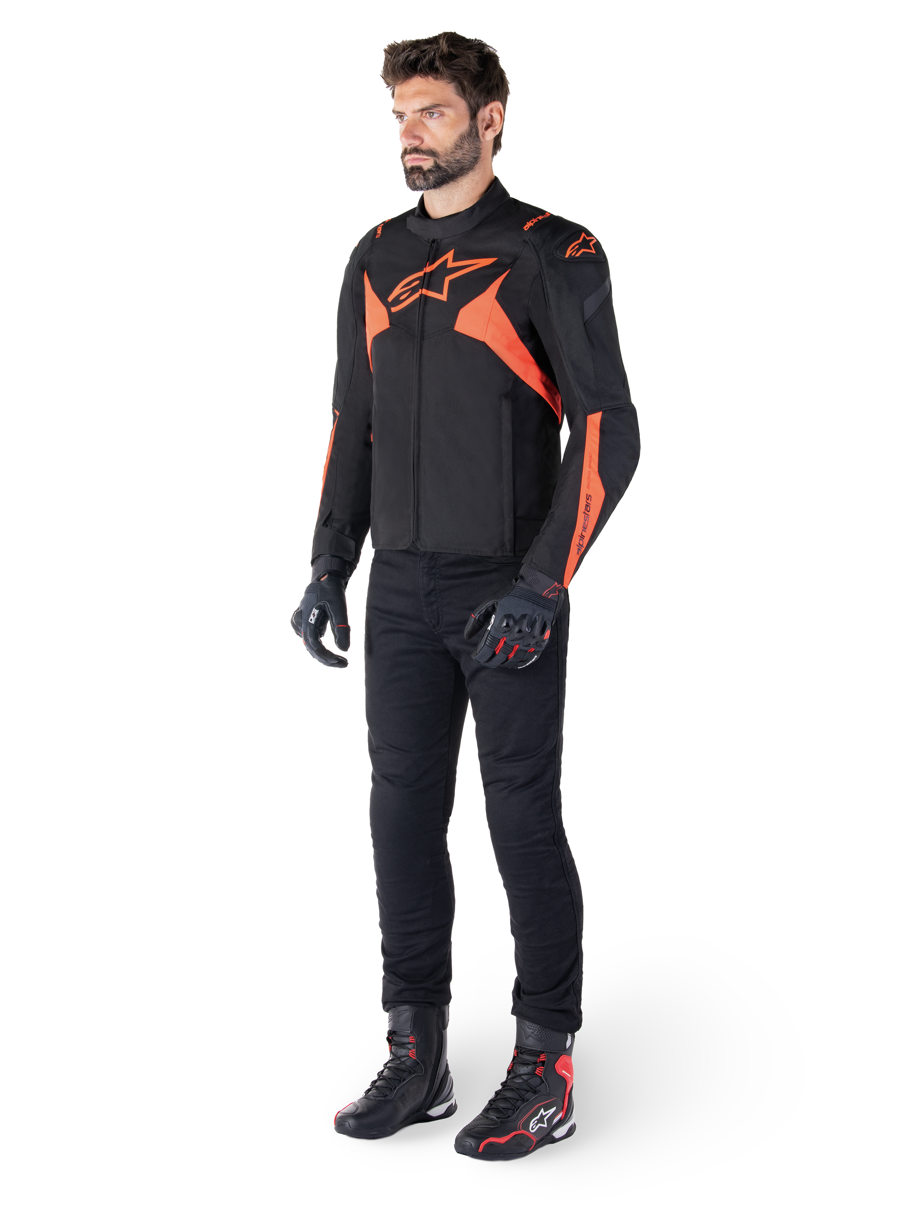 Alpinestars T-Jaws V4 vandtæt jakke, sort og rød fluo, båret af en mandlig model med sorte bukser, handsker og støvler, med klare orange detaljer og Alpinestars-logoet, sporty design til motorcykelkørsel