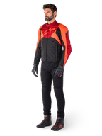 Mandlig rytter iført Alpinestars T-Jaws V4 vandtæt jakke i Sort Rød Fluo Mørkerød, kombineret med sorte motorcykelbukser, handsker og kørestøvler, sport-fit tekstildesign med markant logo på brystet og en aggressiv silhuet.