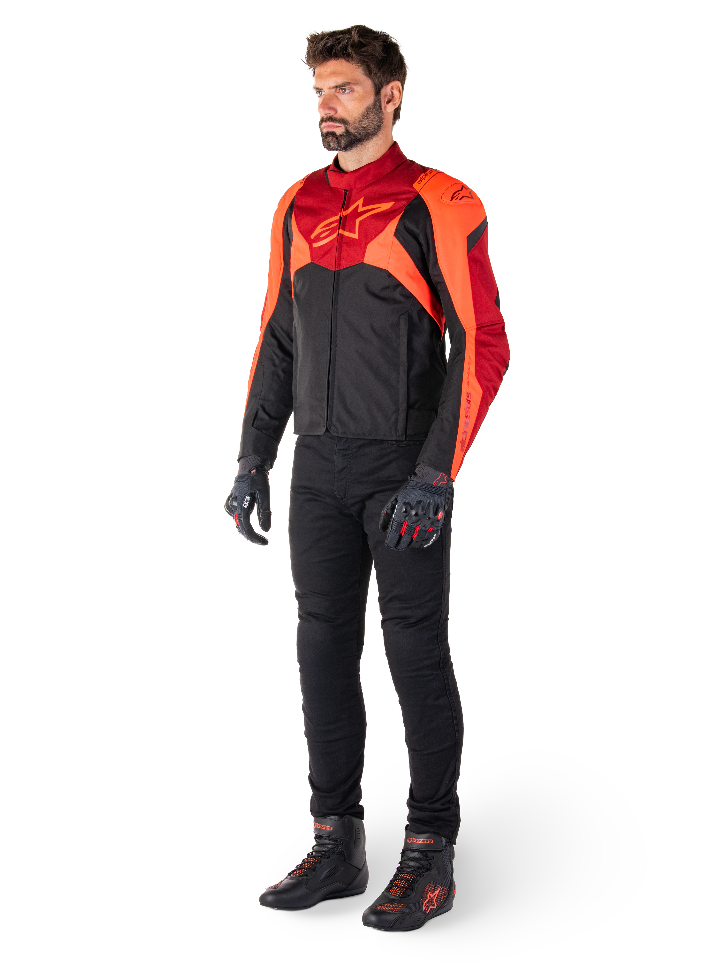 Mandlig rytter iført Alpinestars T-Jaws V4 vandtæt jakke i Sort Rød Fluo Mørkerød, kombineret med sorte motorcykelbukser, handsker og kørestøvler, sport-fit tekstildesign med markant logo på brystet og en aggressiv silhuet.