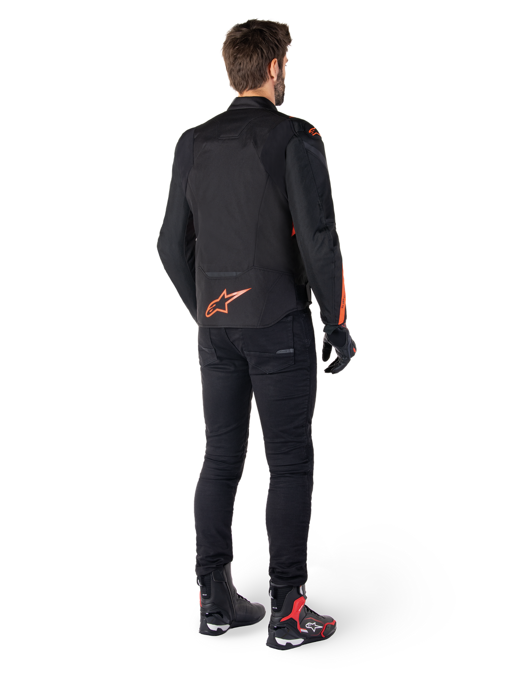 Alpinestars T-Jaws V4 vandtæt jakke, sort og rød fluo, set bagfra på en mandlig kører, med et markant rød fluo logo på ryggen, stylet med sorte kørebukser og tekniske støvler, sportsligt motorcykeludstyr