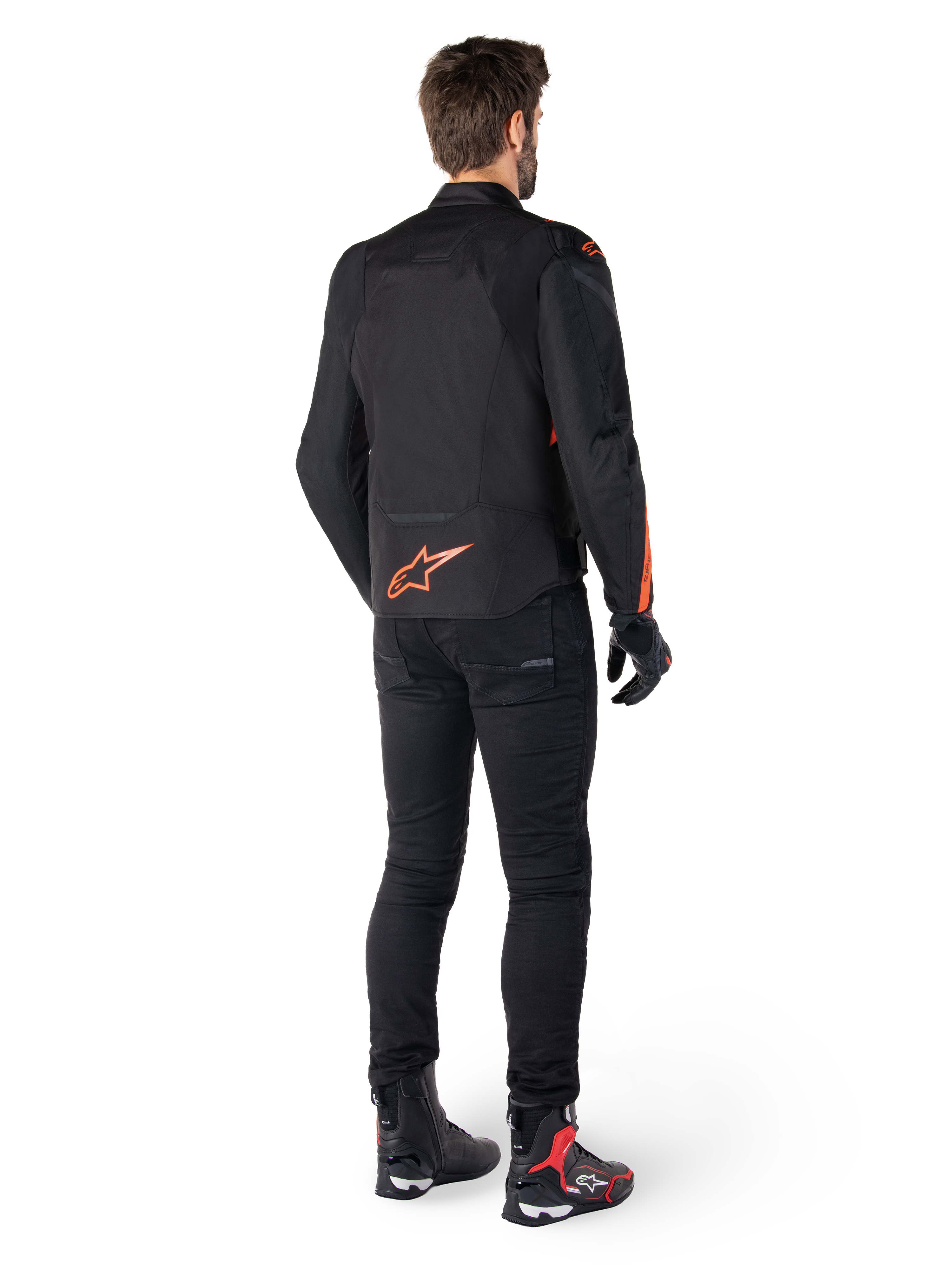 Alpinestars T-Jaws V4 vandtæt jakke, sort og rød fluo, set bagfra på en mandlig kører, med et markant rød fluo logo på ryggen, stylet med sorte kørebukser og tekniske støvler, sportsligt motorcykeludstyr