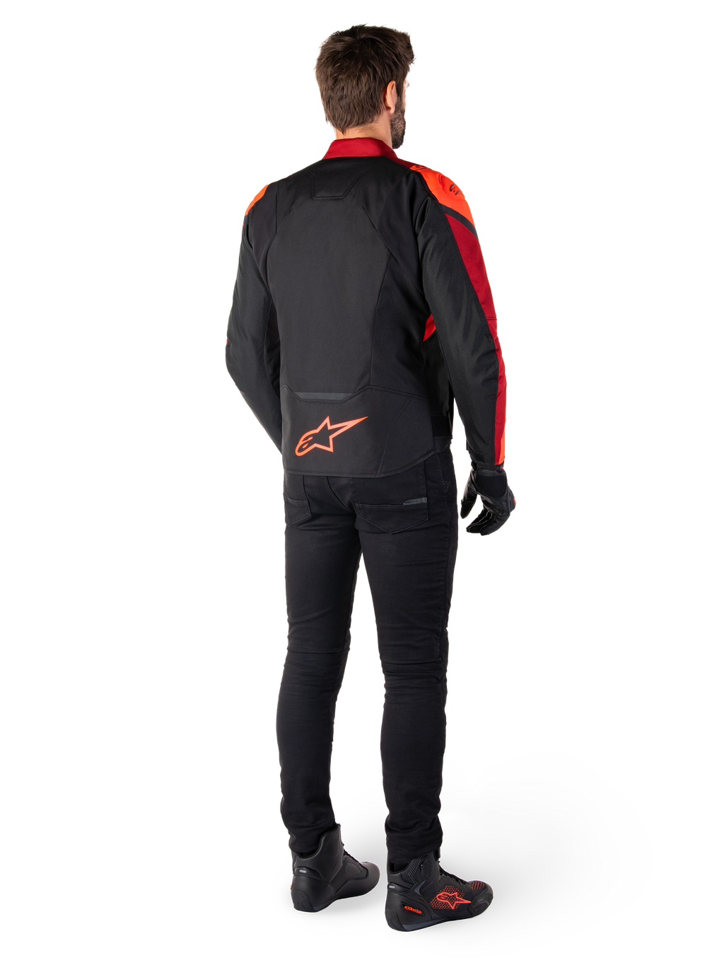 Alpinestars T-Jaws V4 vandtæt jakke i sort, rød fluo og mørkerød, set bagfra på en kører iført tekstiljakken med sorte bukser og kørselstøvler, med et markant rødt Alpinestars-logo nederst på ryggen.