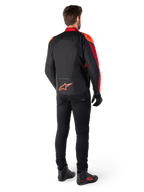 Alpinestars T-Jaws V4 vandtæt jakke i sort, rød fluo og mørkerød, set bagfra på en kører iført tekstiljakken med sorte bukser og kørselstøvler, med et markant rødt Alpinestars-logo nederst på ryggen.