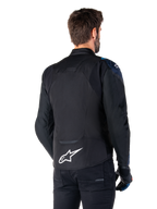 Alpinestars T-Jaws V4 Waterproof Jacket, set bagfra, sort med mørkeblå og Blithe Blue-detaljer, hvidt stjernelogo på lænden, sportslig silhuet, bæres med sorte bukser og kørehandsker