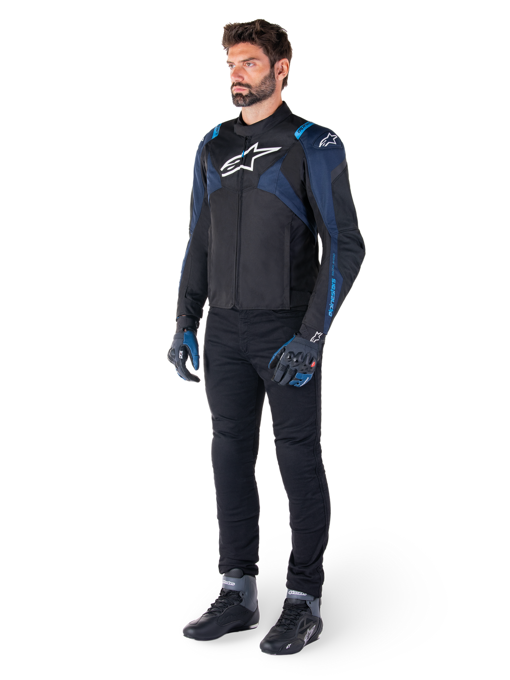 Alpinestars T-Jaws V4 vandtæt jakke, sort, mørkeblå og Blithe Blue, båret af en model med sorte motorcykelbukser og kørestøvler, hvidt Alpinestars-logo på brystet og blå skulderdetaljer, sport-fit køreudstyr